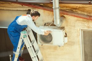 HVAC technician working on a capacitor part for condensing unit. Male worker or repairman in uniform repairing and adjusting conditioning system, diagnosting and looking for technical issues.